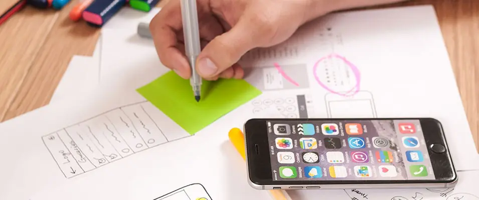 Profissional planejando layout mobile first em esboço de site responsivo com smartphone sobre a mesa