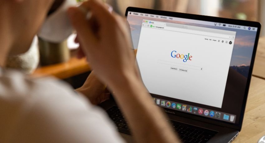 Pessoa usando um notebook com a página inicial do Google aberta no navegador enquanto segura uma xícara.