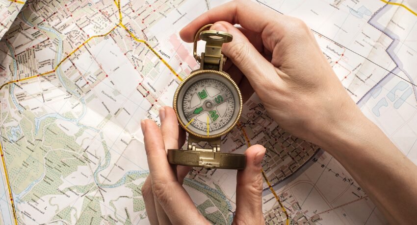 Mapa aberto com uma bússola dourada sendo segurada por duas mãos, simbolizando o início da jornada do cliente e o processo de orientação em cada etapa.