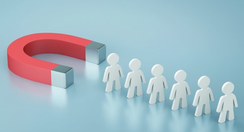 Ímã vermelho em formato de ferradura atraindo uma fila de figuras humanas brancas, representando atração de clientes.